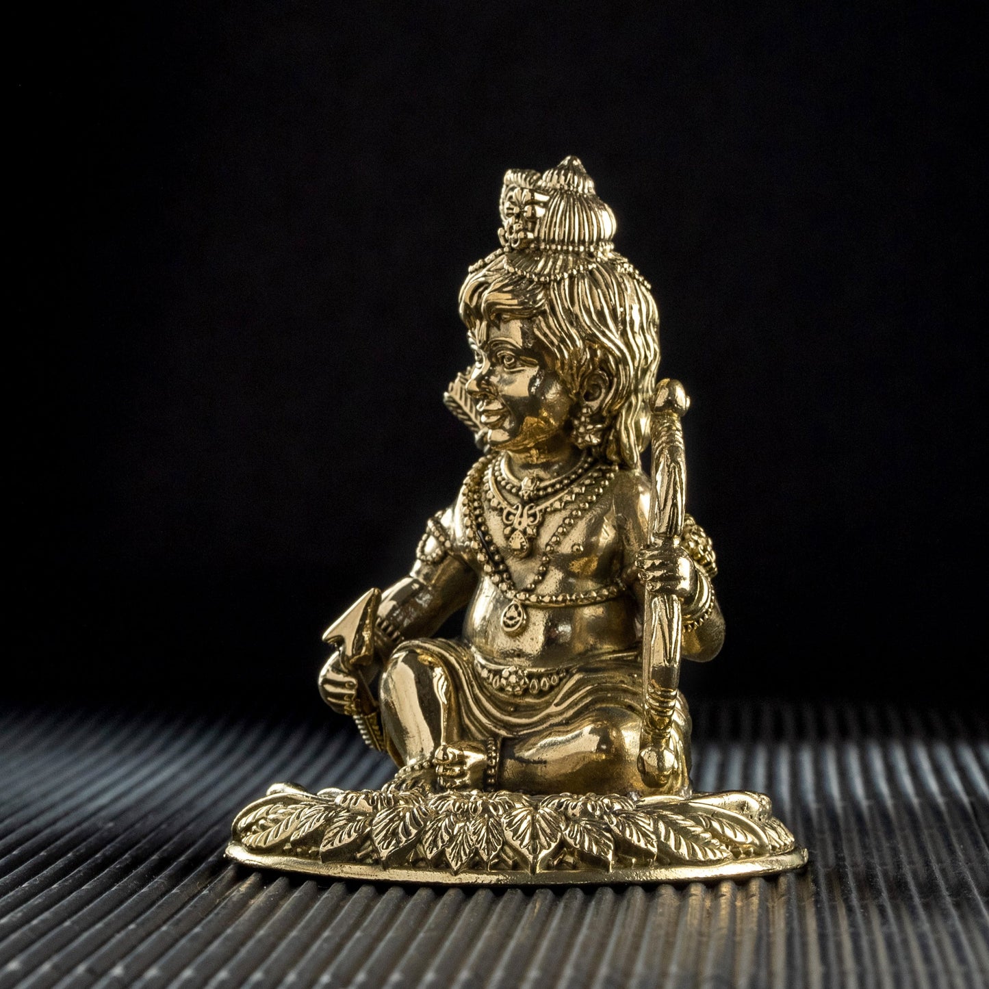 Brass statue of a seated figure on a textured surface with a black background