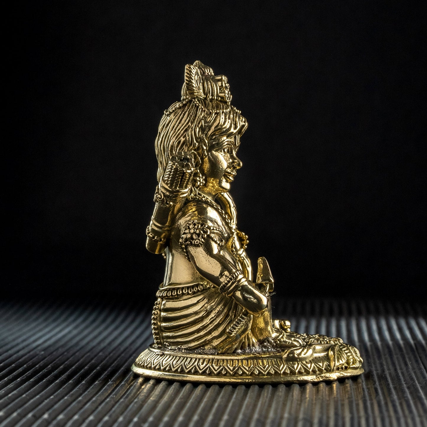Bronze statue of a seated figure on a textured surface with a black background