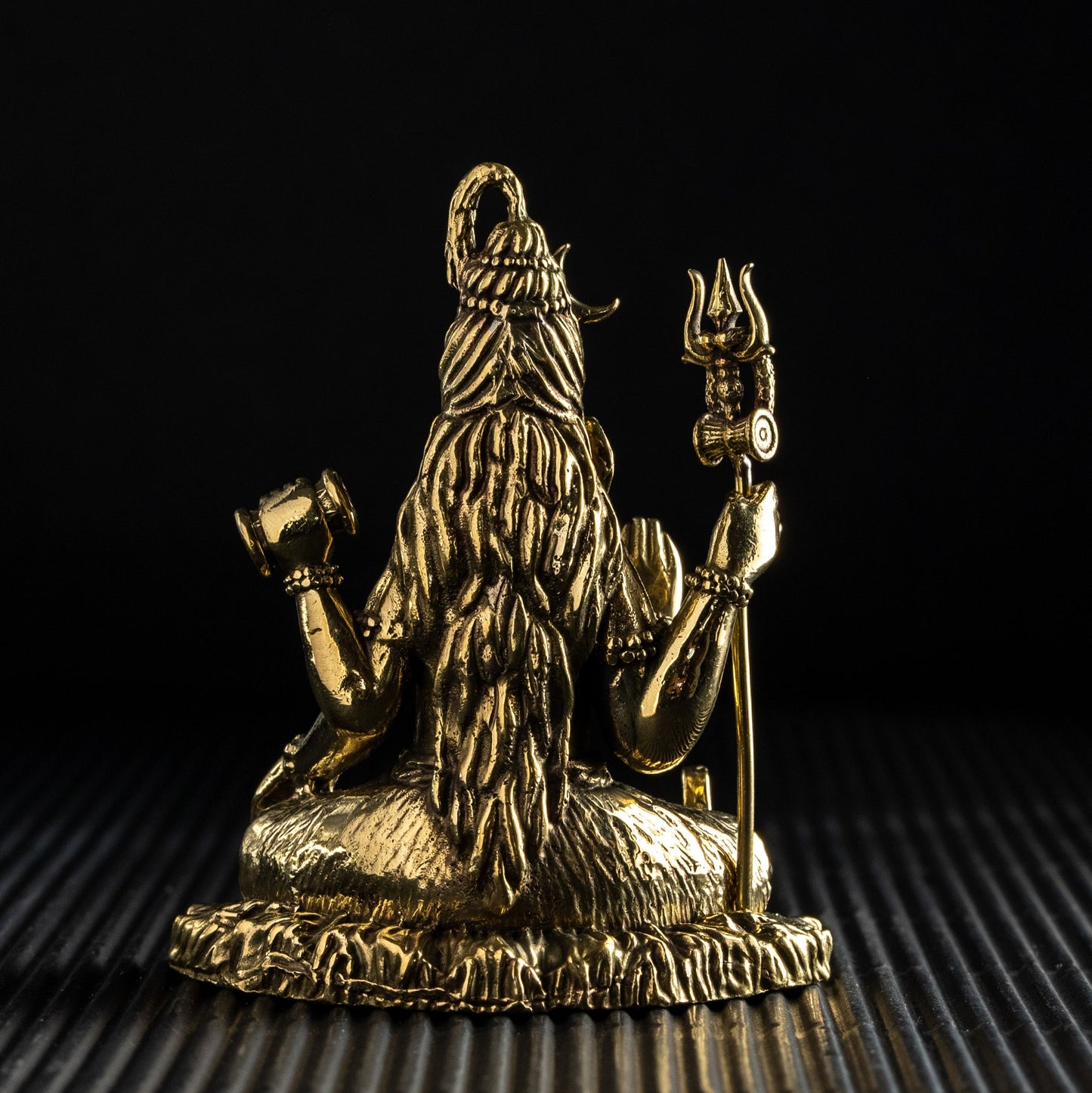 Gold-colored statue of a deity on a textured surface with a black background