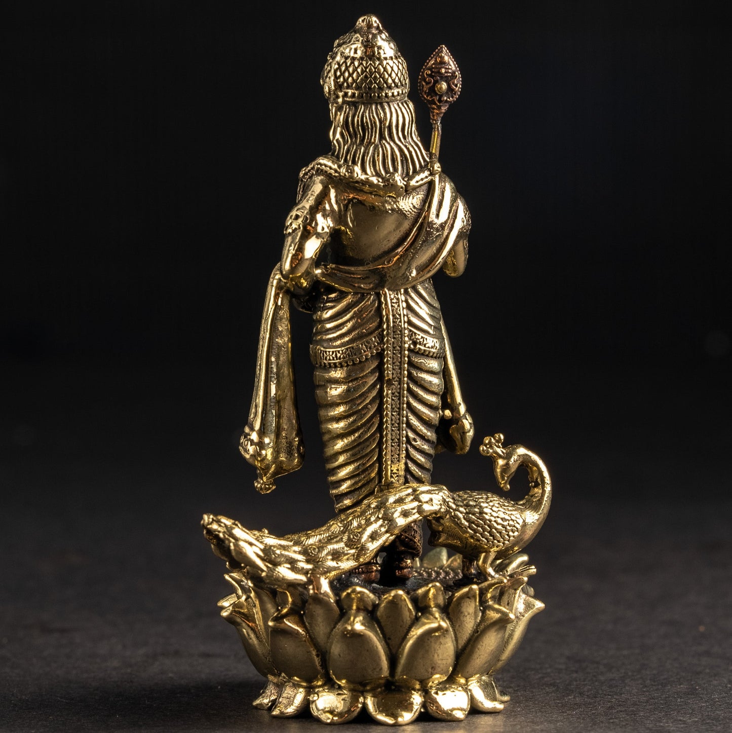 Gold-colored statue of a deity on a lotus flower against a black background
