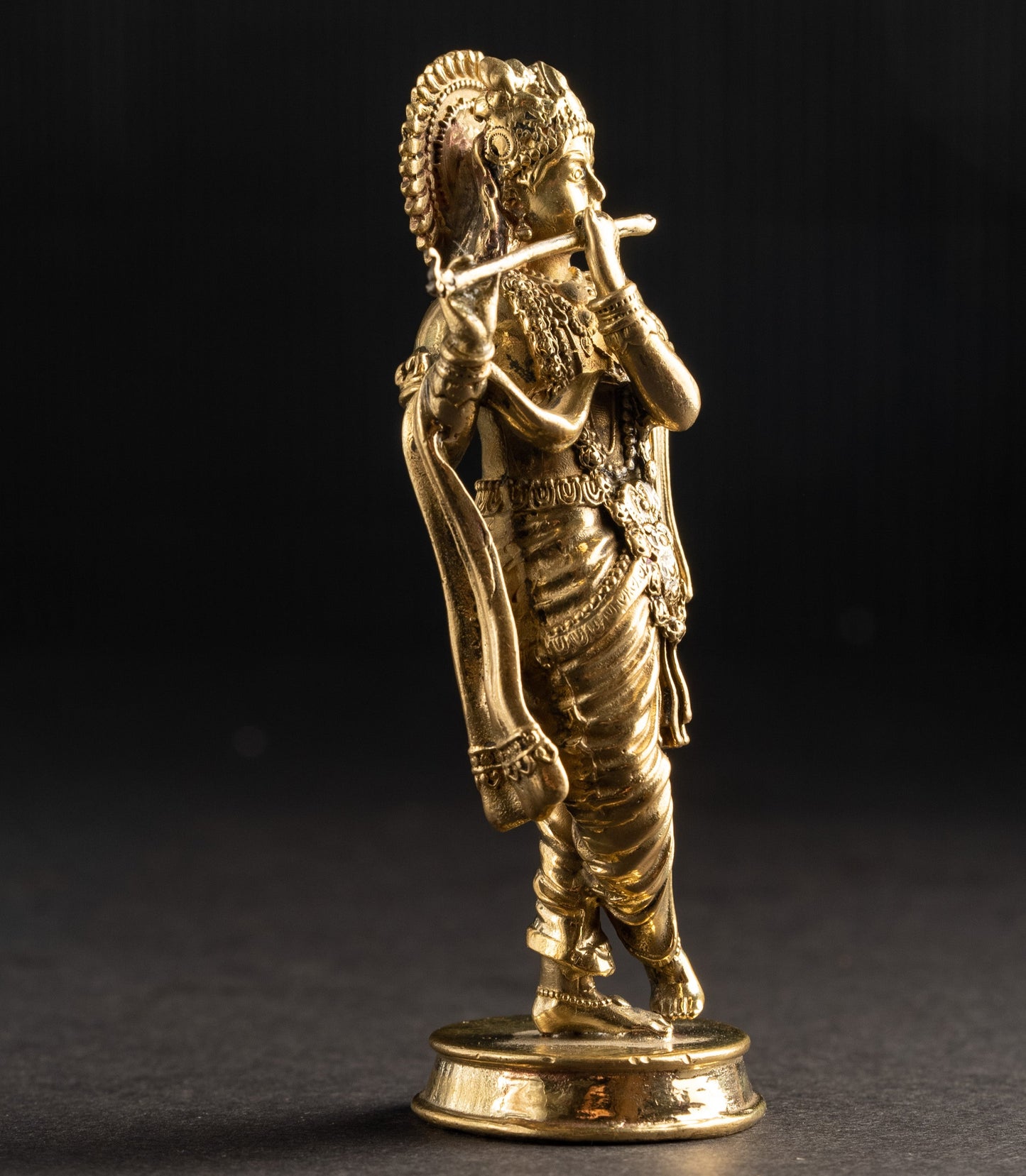Gold-colored statue of a figure with a headdress on a dark background