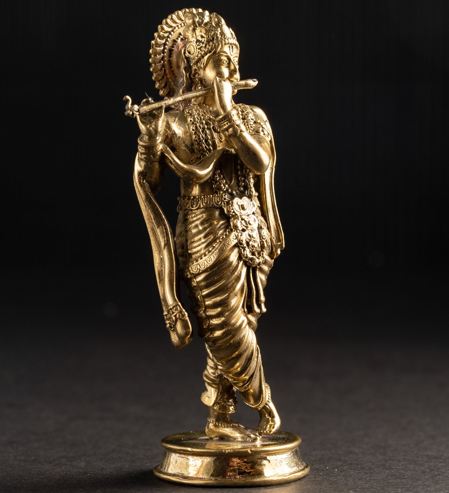 Gold statue of a deity playing a flute on a black background