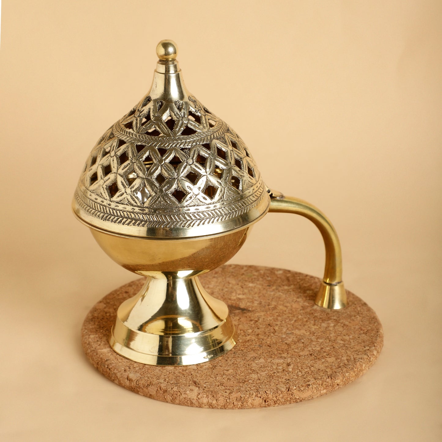 Decorative brass incense burner on a cork base against a beige background