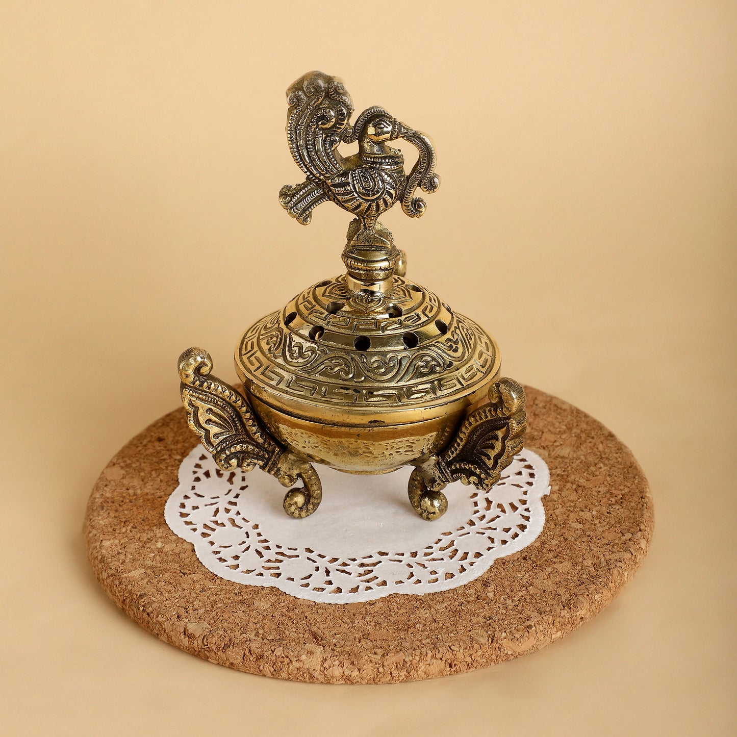 Decorative brass incense burner on a cork coaster with a white doily underneath
