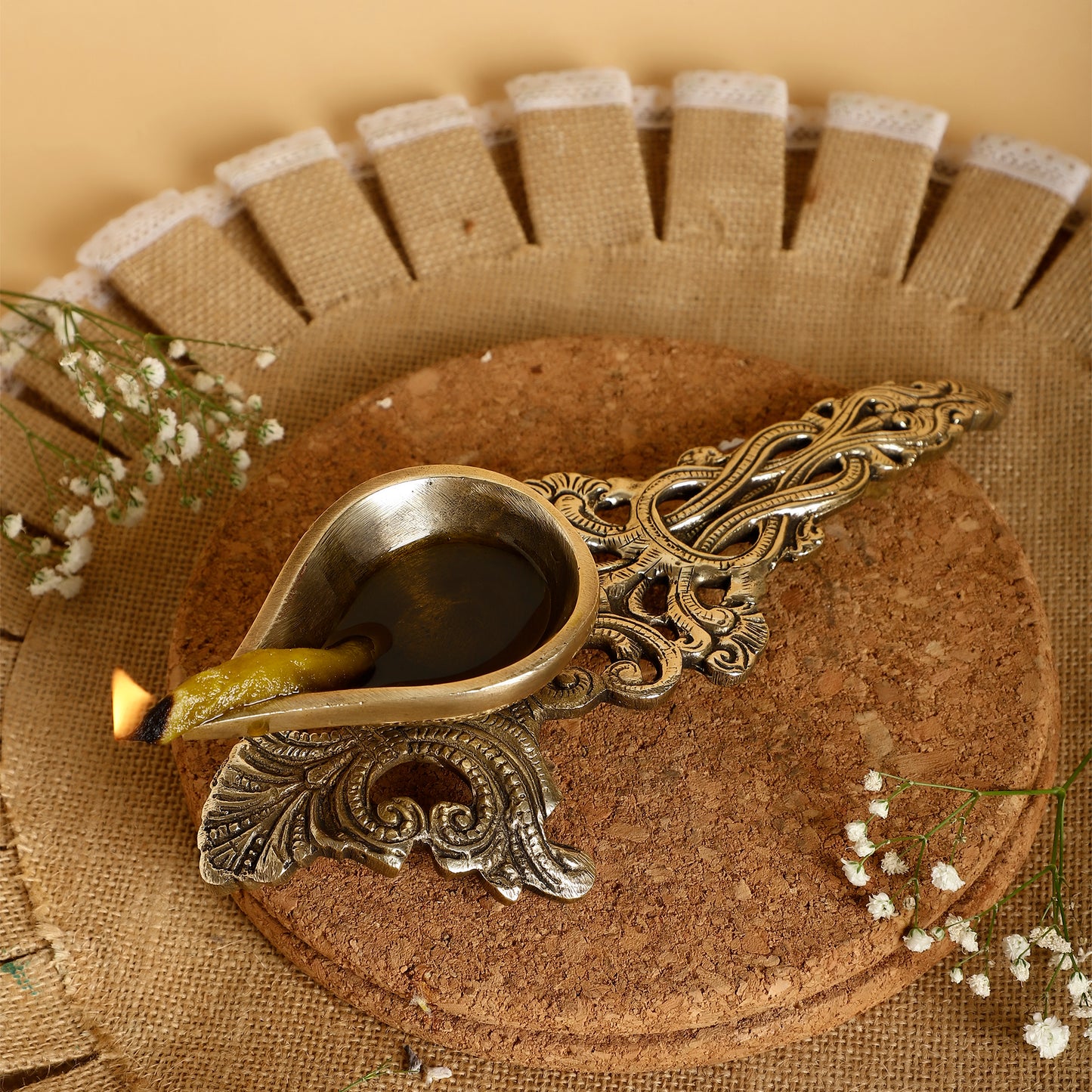 Decorative oil lamp with intricate design on a textured surface with flowers.