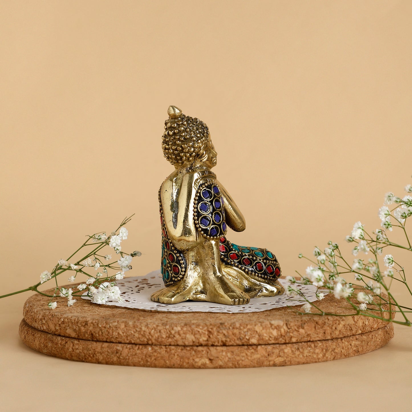 Decorative statue of a seated figure with gemstone details on a cork base with flowers.