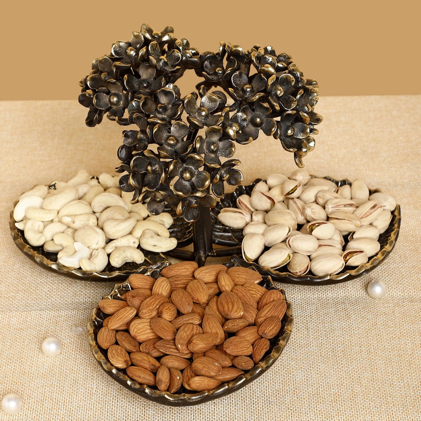 Decorative metal tree with three trays of nuts on a beige background