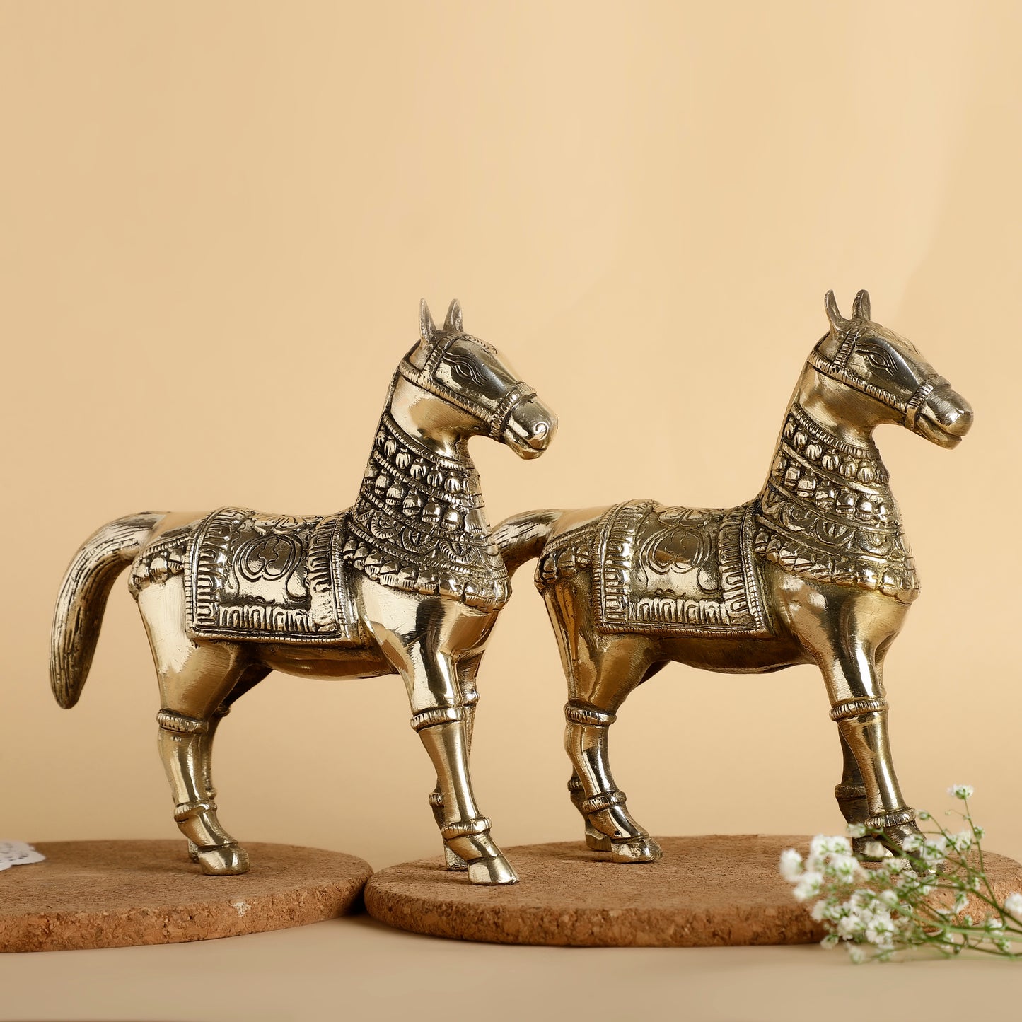 Two ornate brass horse statues on a beige background