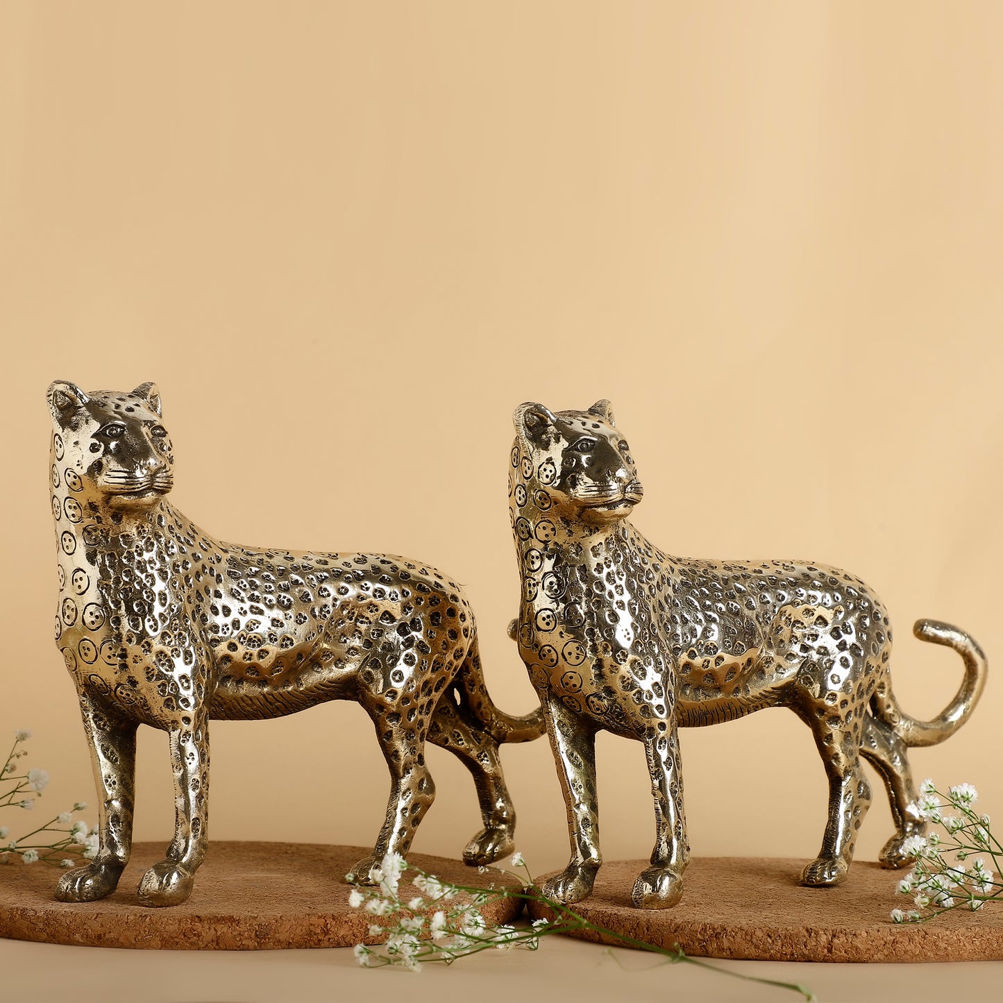 Two metallic leopard sculptures on a beige background