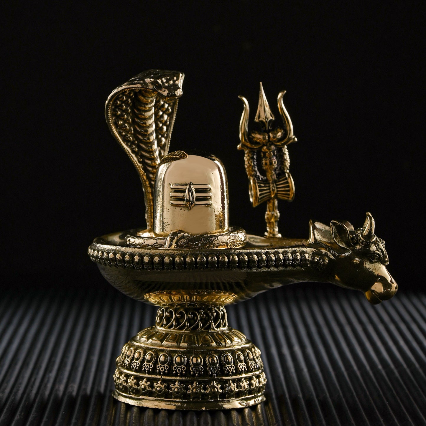 Decorative brass sculpture with snake, trident, and lion on a black background