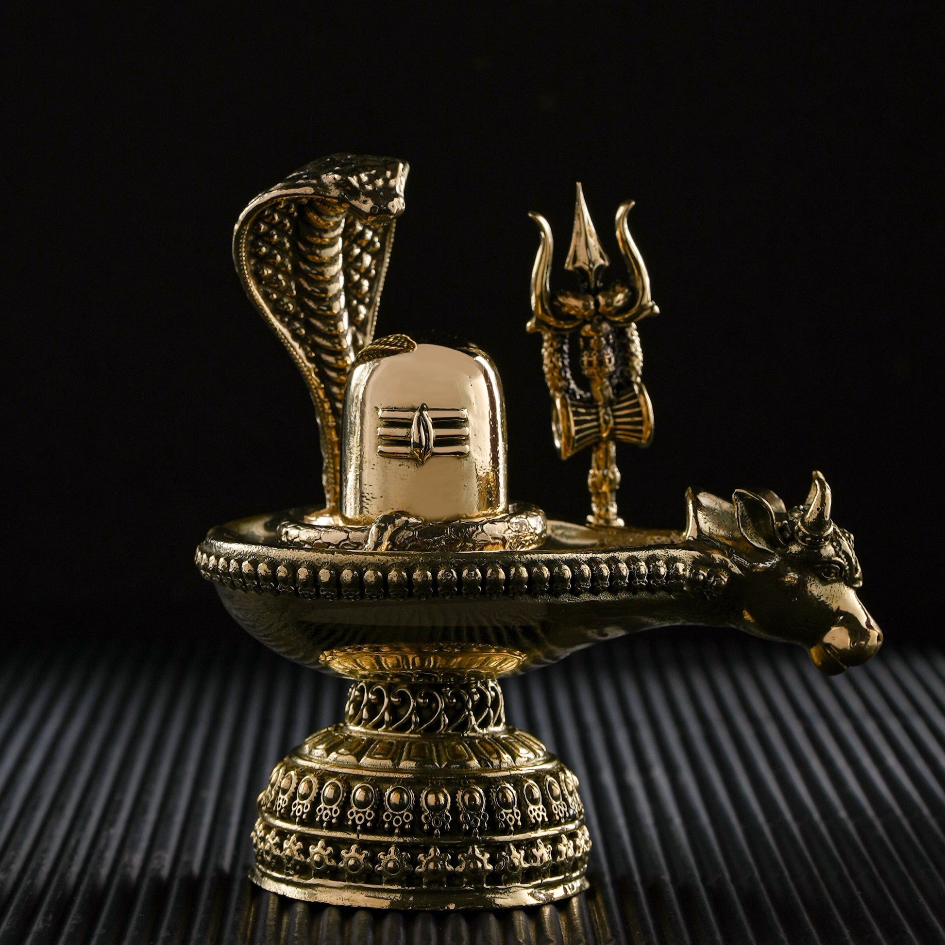 Decorative brass sculpture with snake, trident, and lion on a black background
