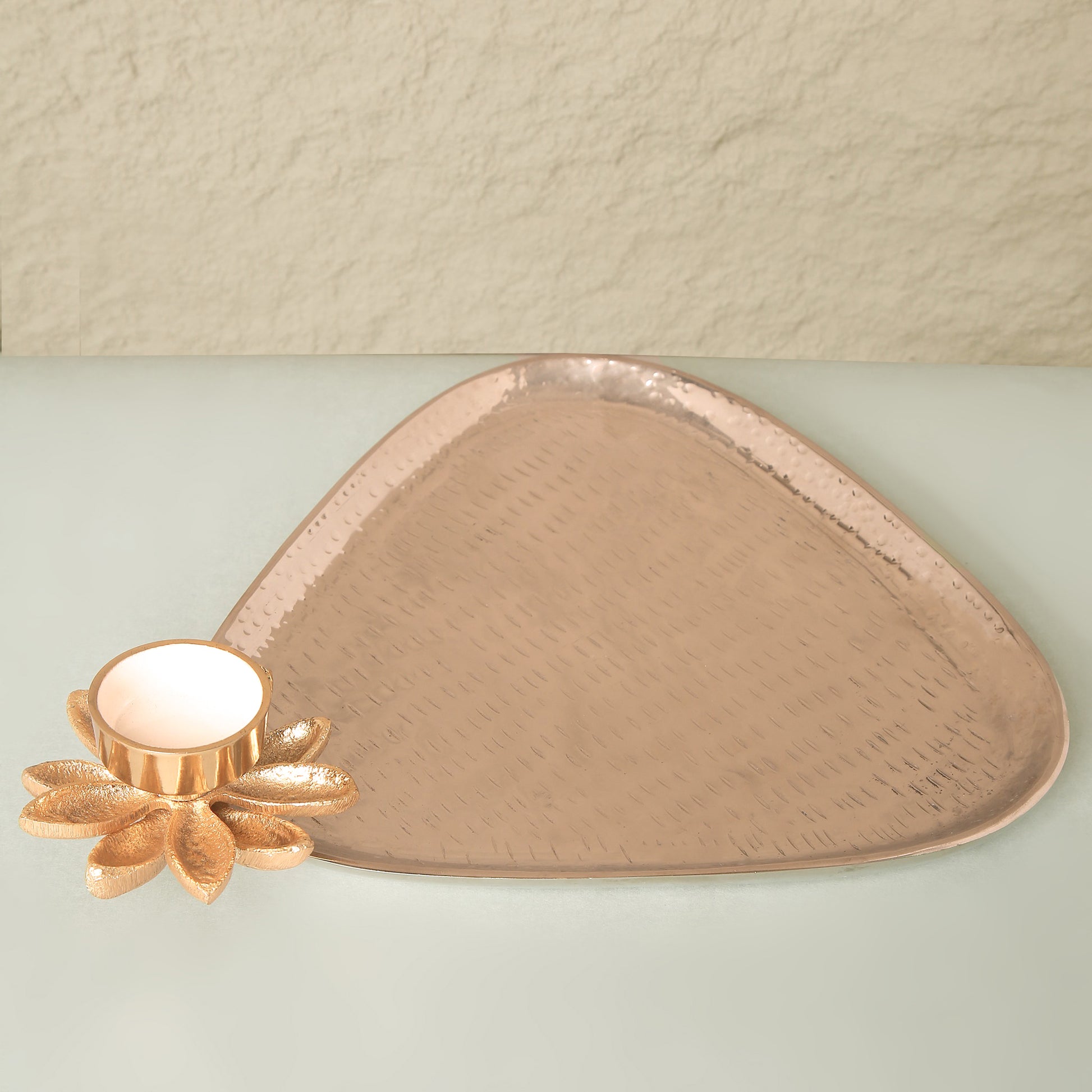 Triangular copper tray with floral design on a light green surface