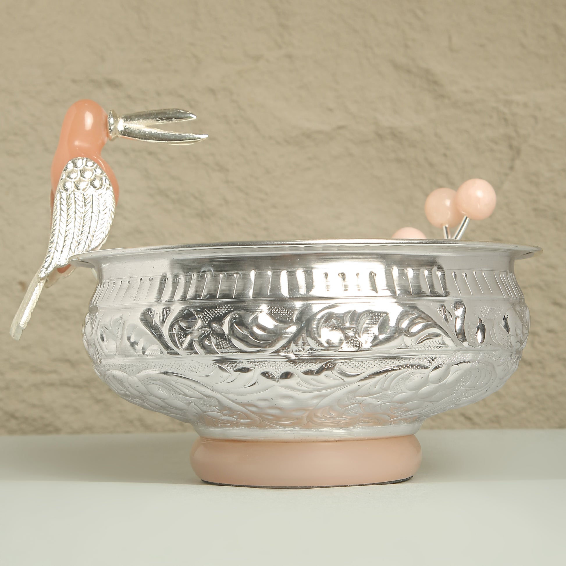 Decorative silver bowl with pink bird figurines on a beige background