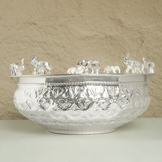 Decorative silver bowl with intricate patterns and small elephant figurines on a beige background