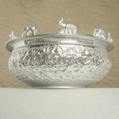 Decorative silver bowl with intricate patterns and small figurines on a beige background
