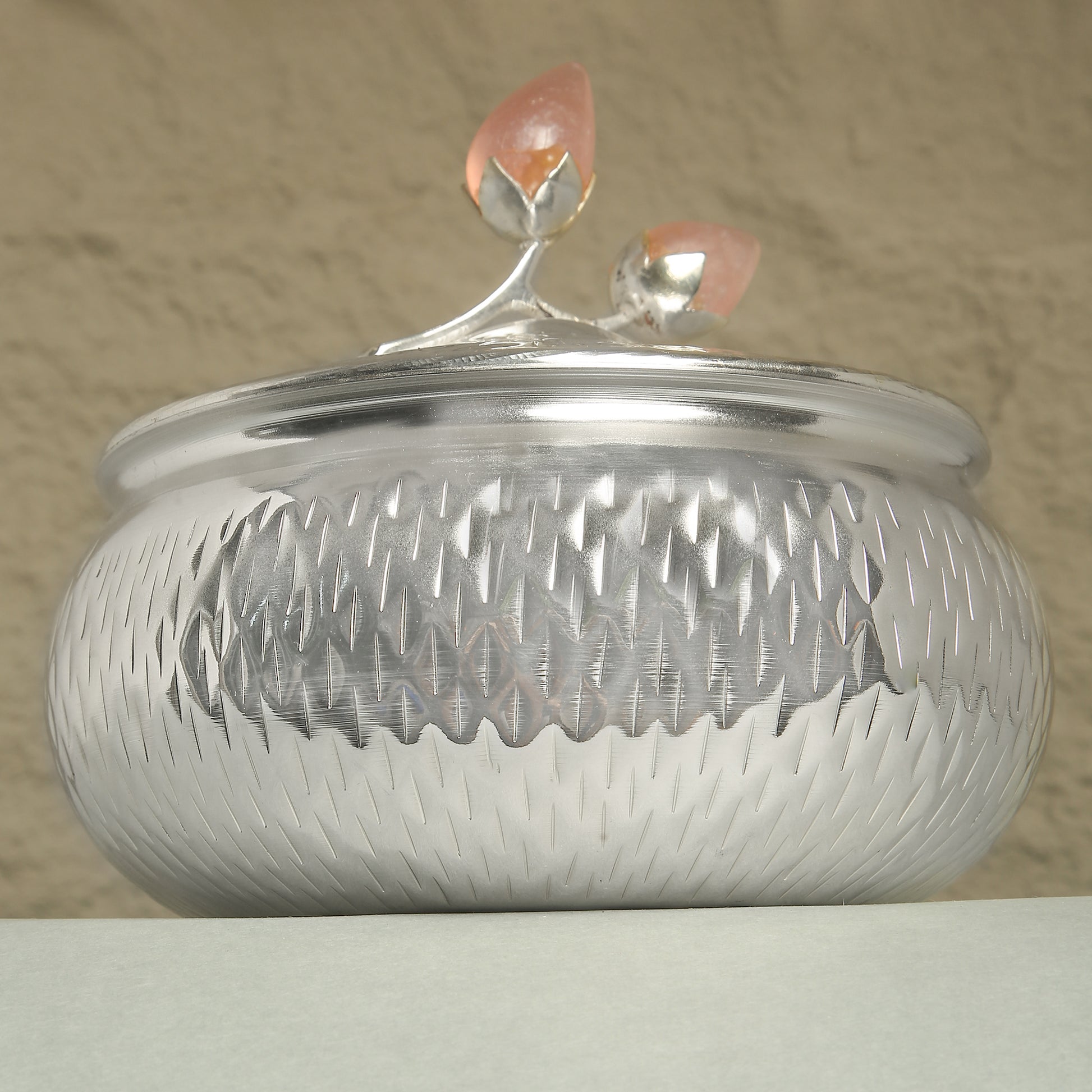 Silver textured container with a decorative lid on a beige background