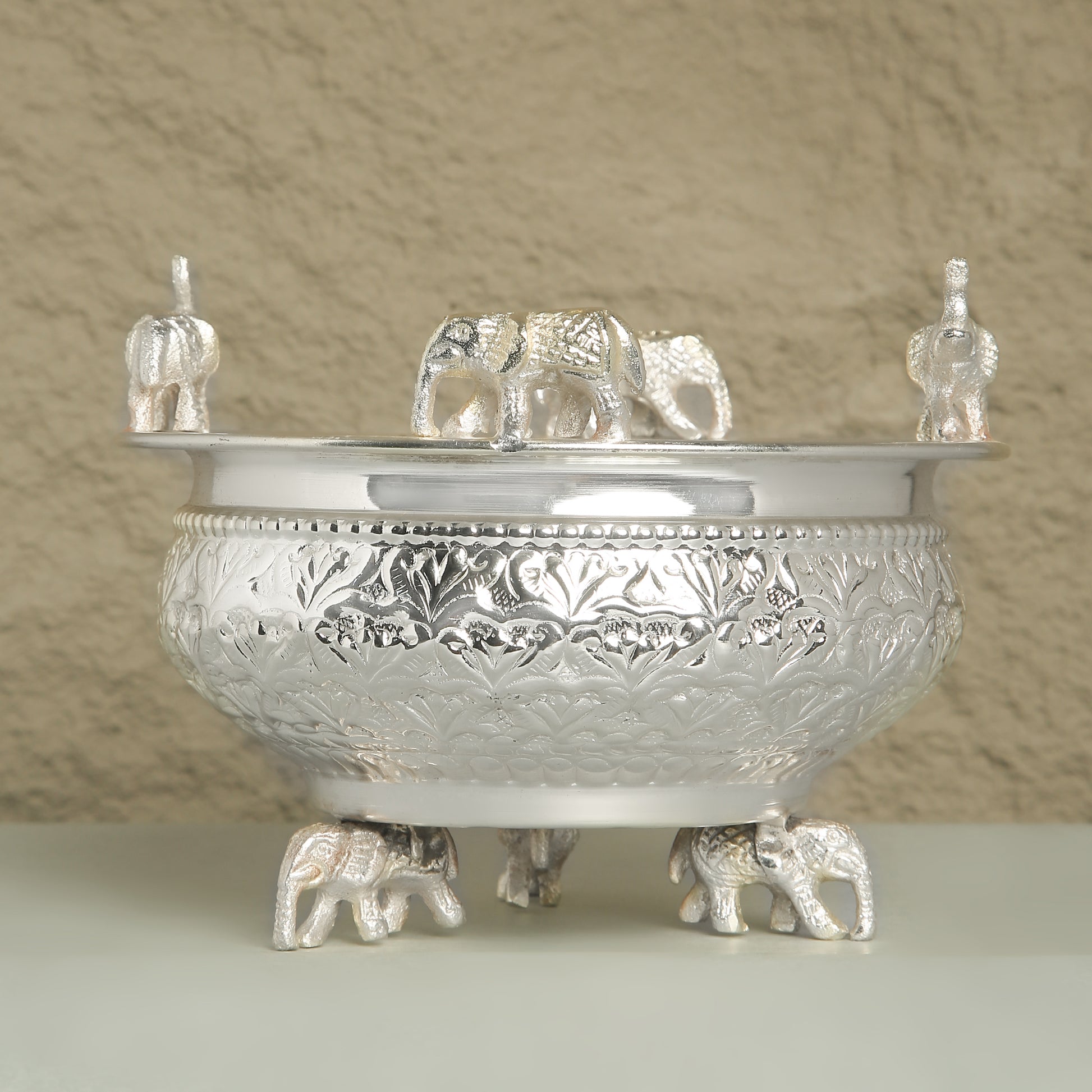 Decorative silver bowl with elephant designs on a neutral background