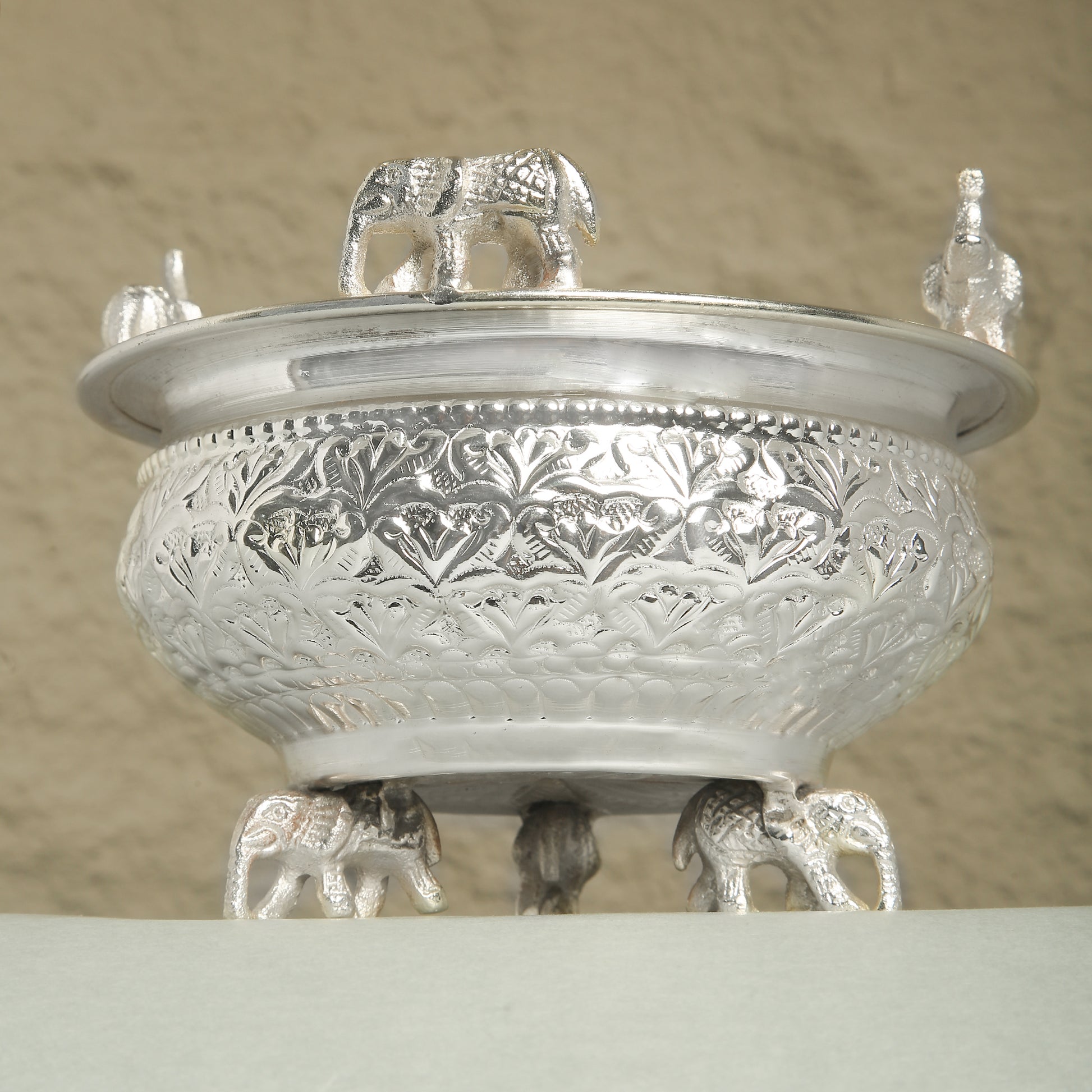 Decorative silver bowl with elephant design on a beige background