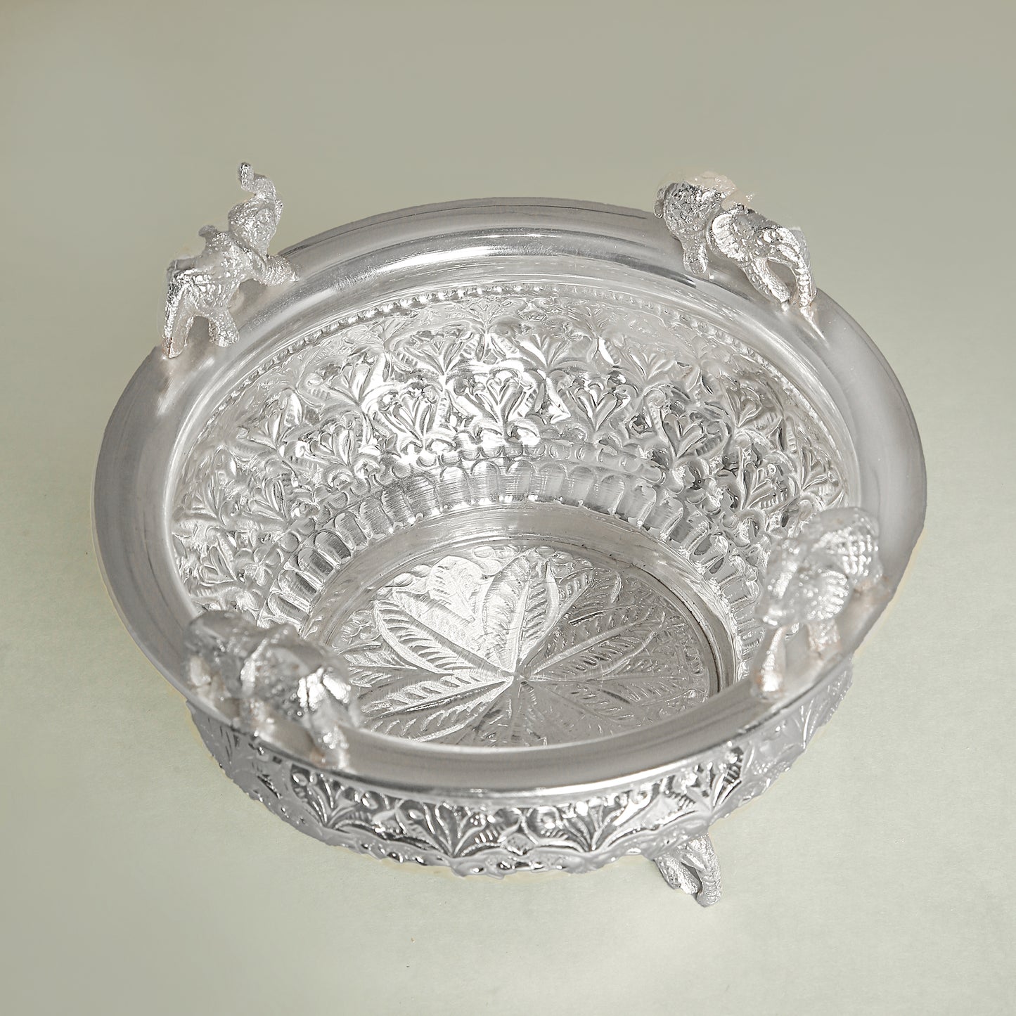 Decorative silver bowl with intricate designs on a light green background