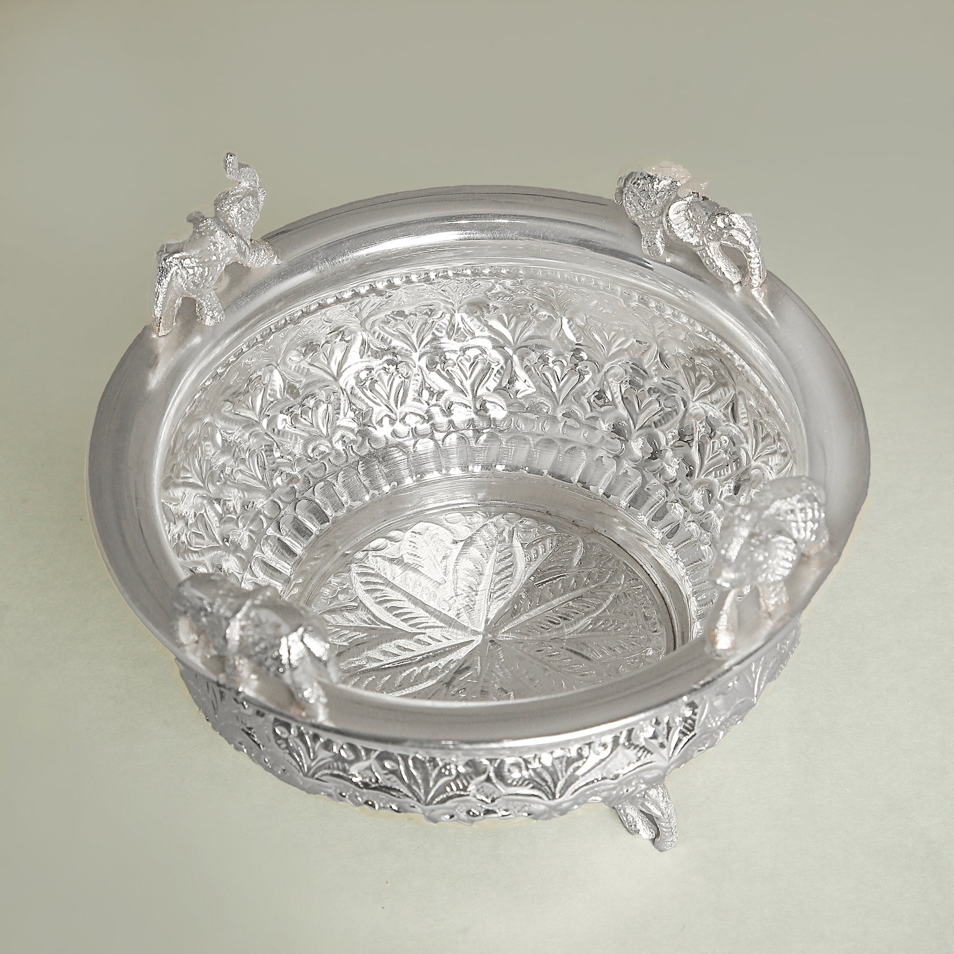 Decorative silver bowl with intricate designs on a light green background