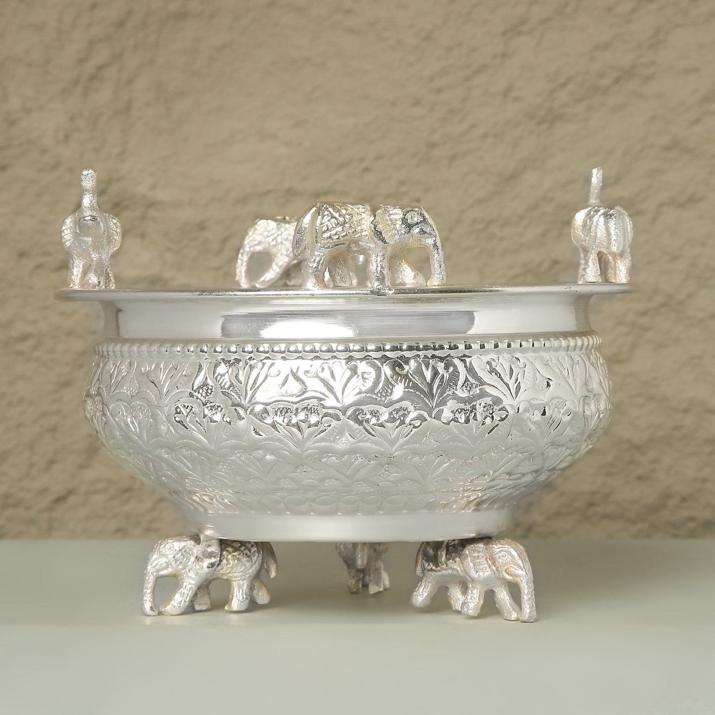 Decorative silver bowl with elephant figures on a beige background