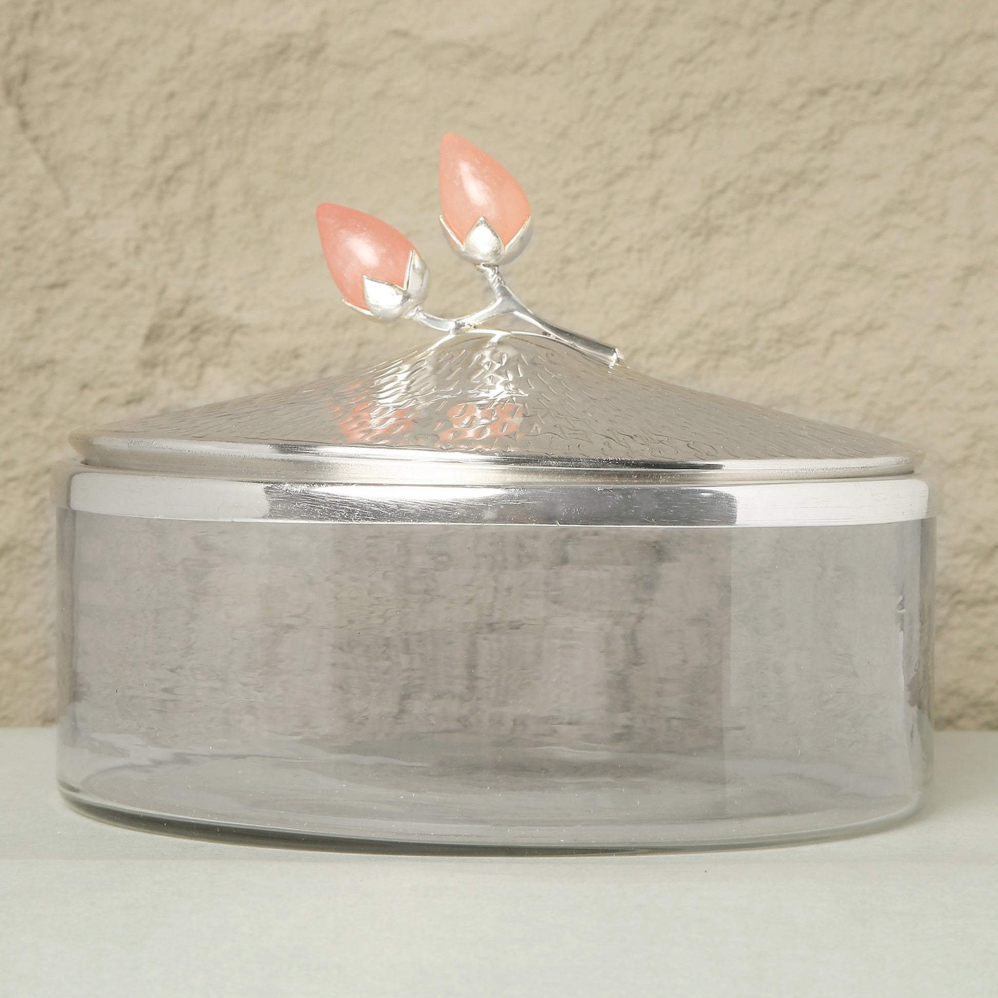 Clear glass container with a silver lid featuring coral-colored handles on a beige background