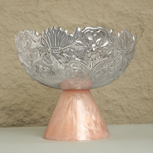 Decorative silver bowl with intricate designs on a pink pedestal against a beige background