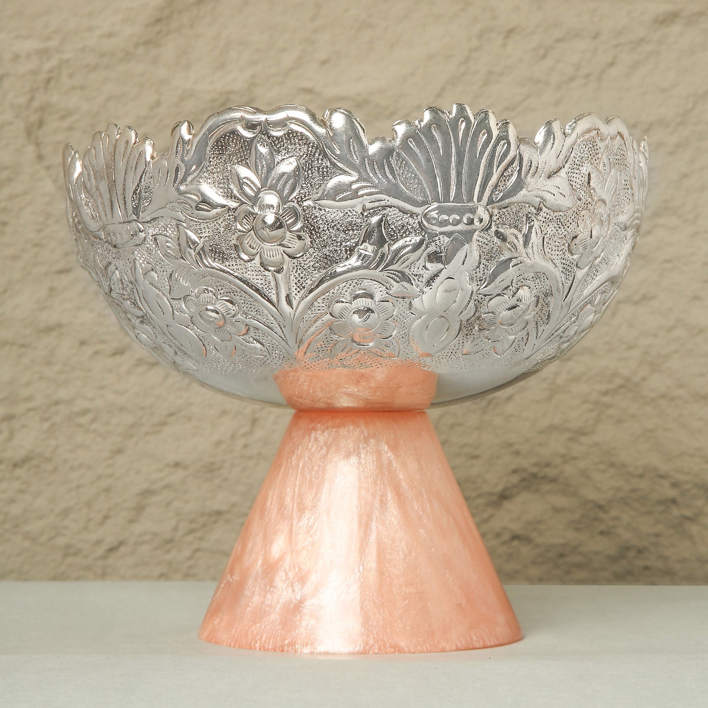 Decorative silver bowl on a pink stand against a beige background