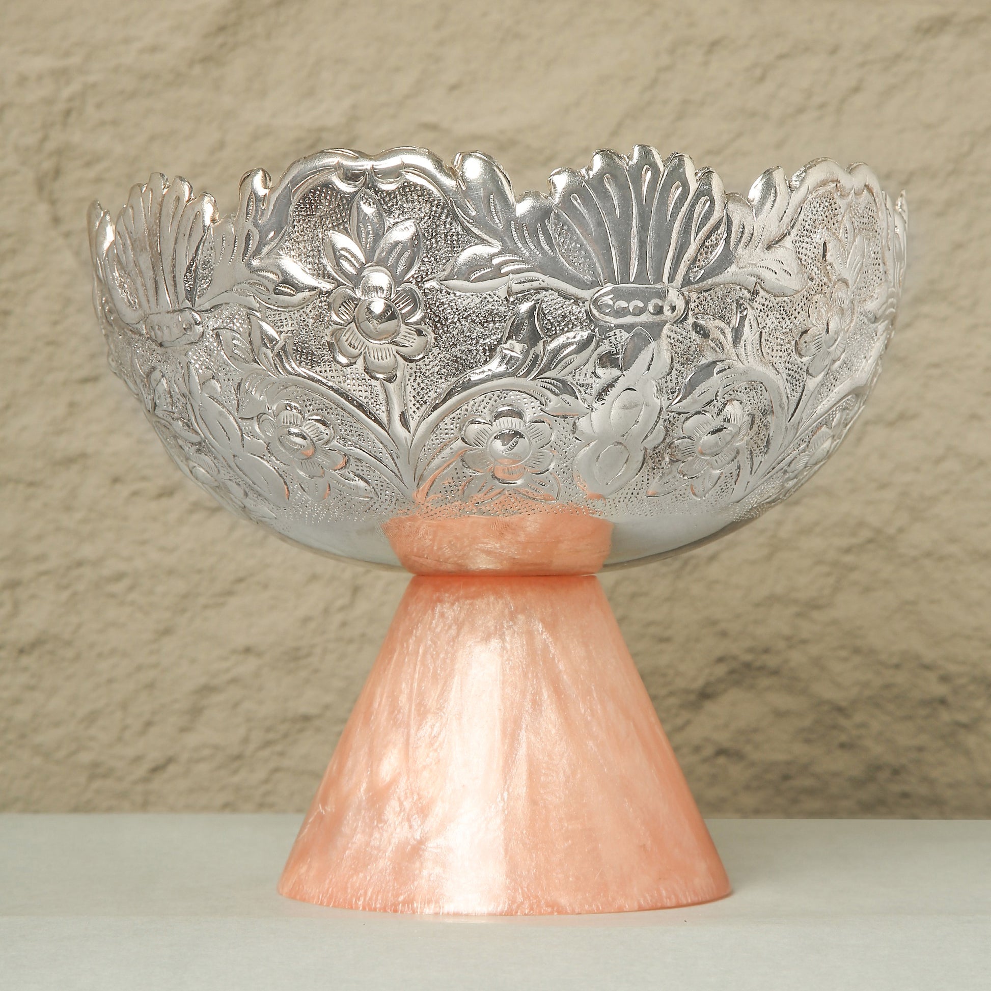 Decorative silver bowl on a pink stand against a beige background