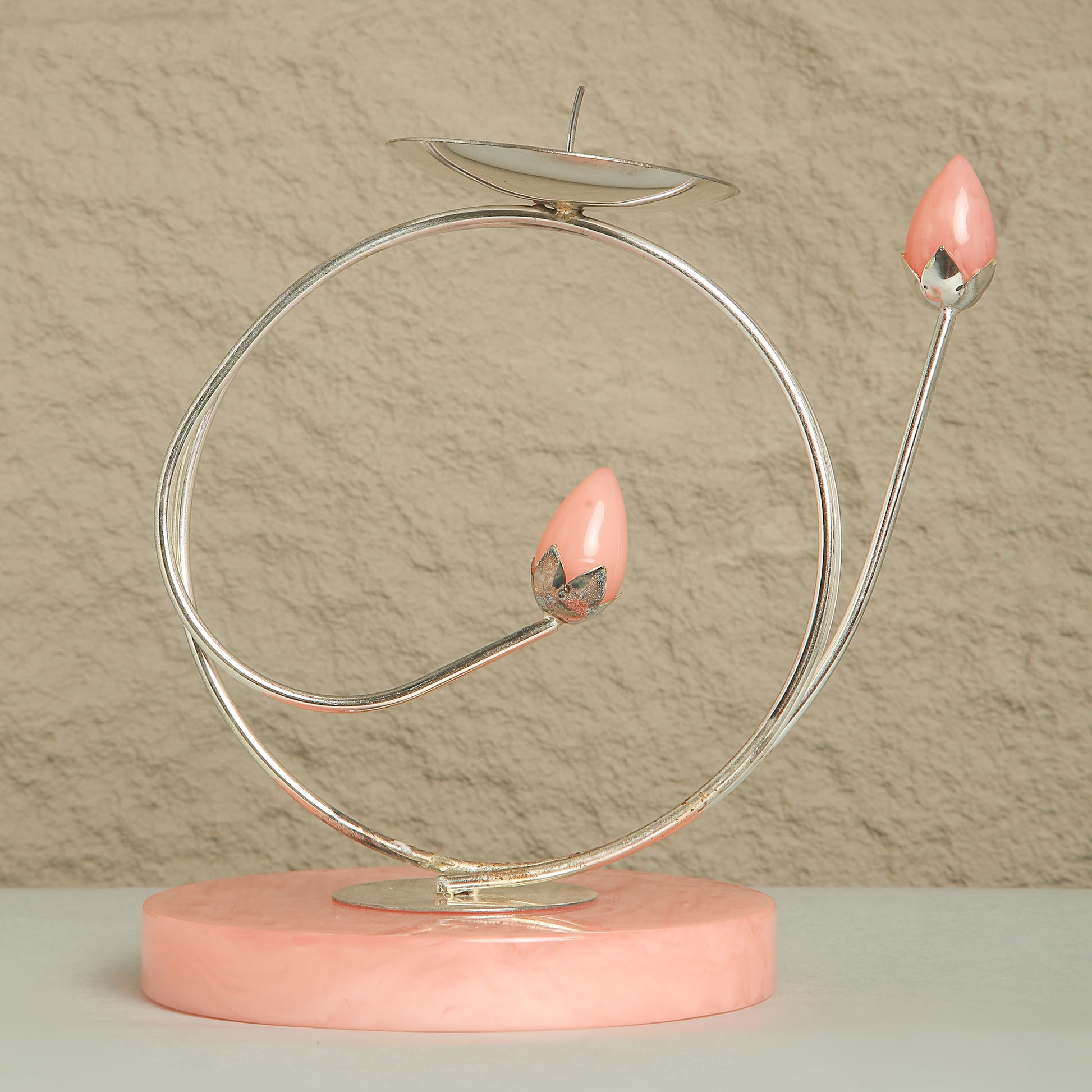 Decorative item with pink candle-like objects on a circular metal stand against a beige background
