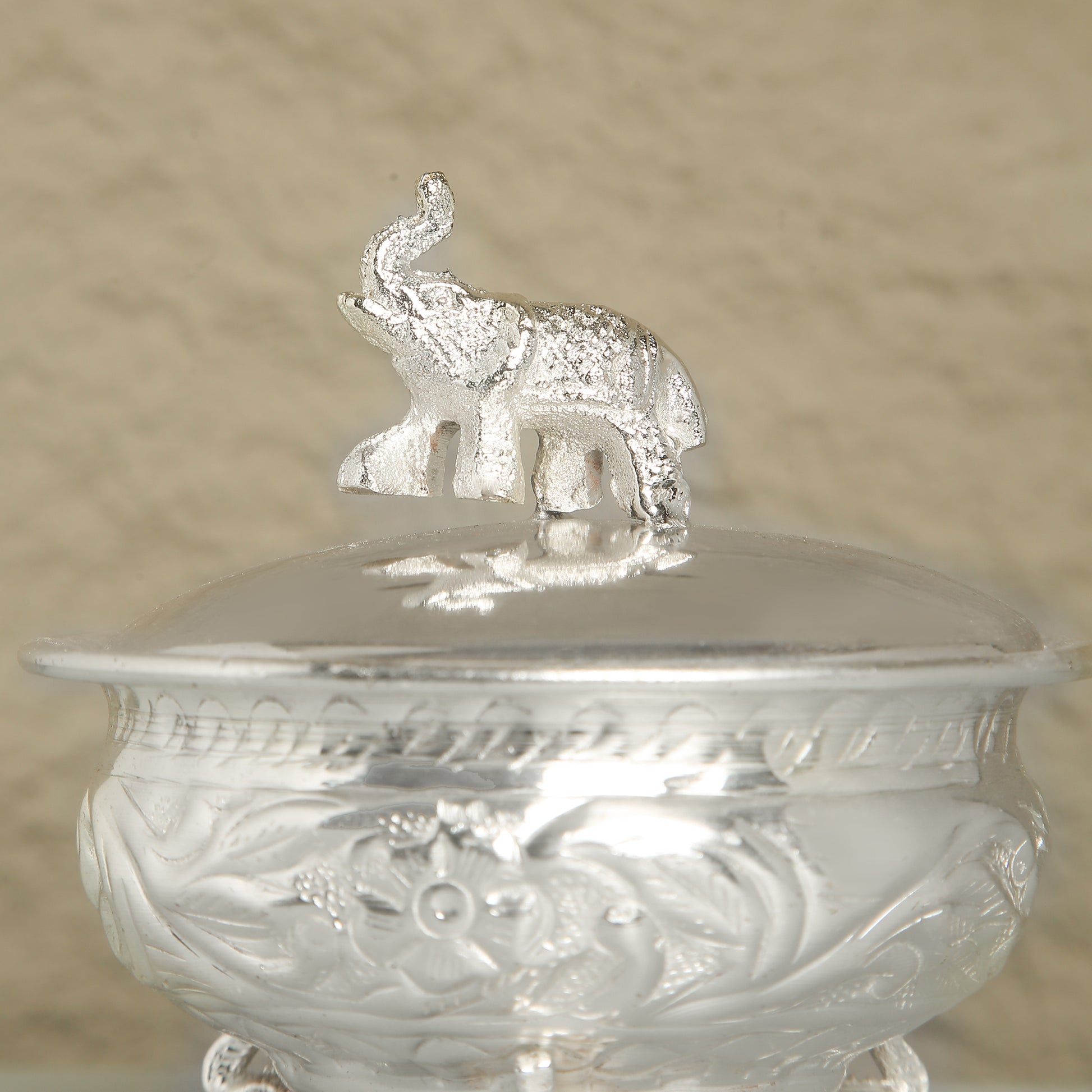 Silver container with an elephant on top against a beige background