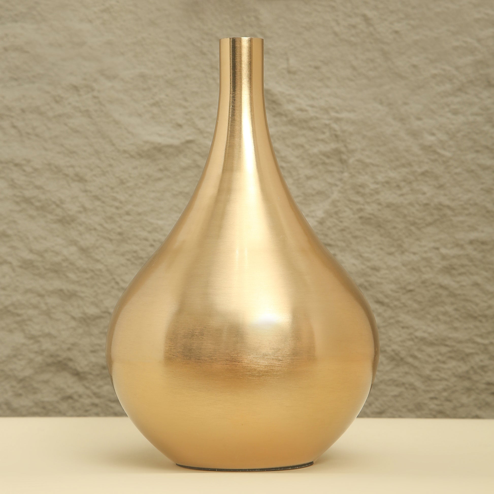 Gold vase on a beige surface with a textured brown wall background