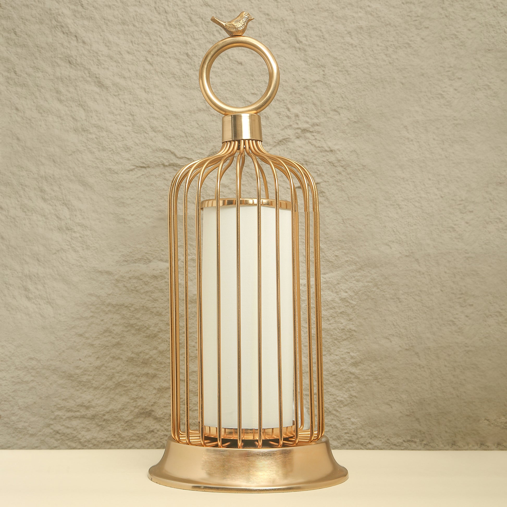 Gold birdcage-shaped lantern with a white candle on a beige background