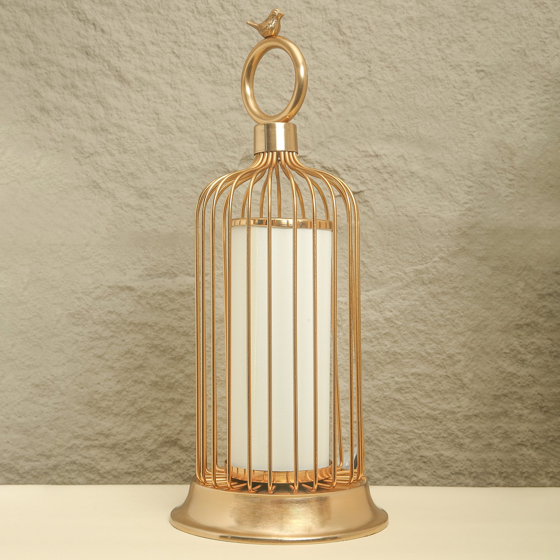 Gold birdcage-style lantern with a white candle on a textured beige background