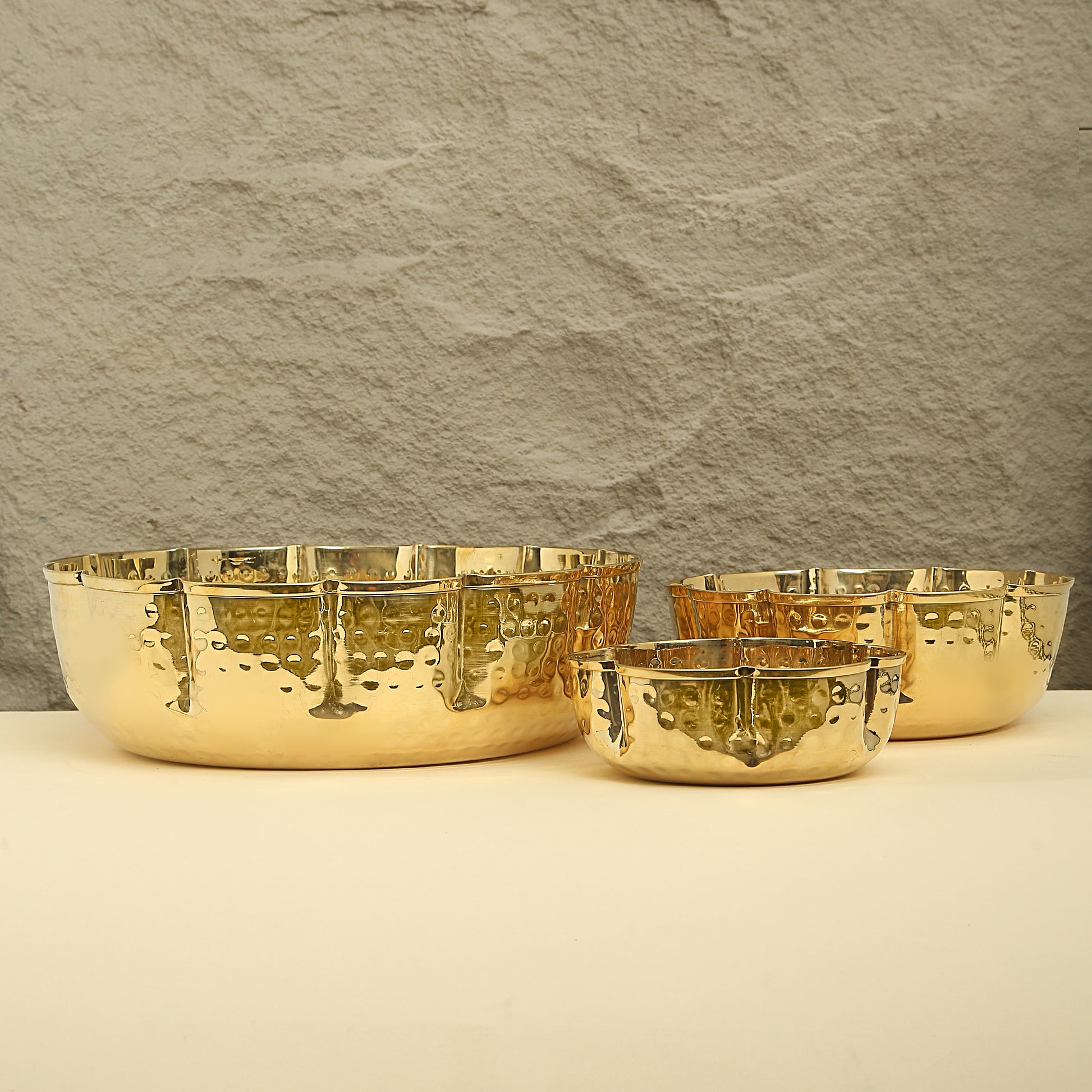 Set of gold bowls on a beige surface with a textured gray wall background