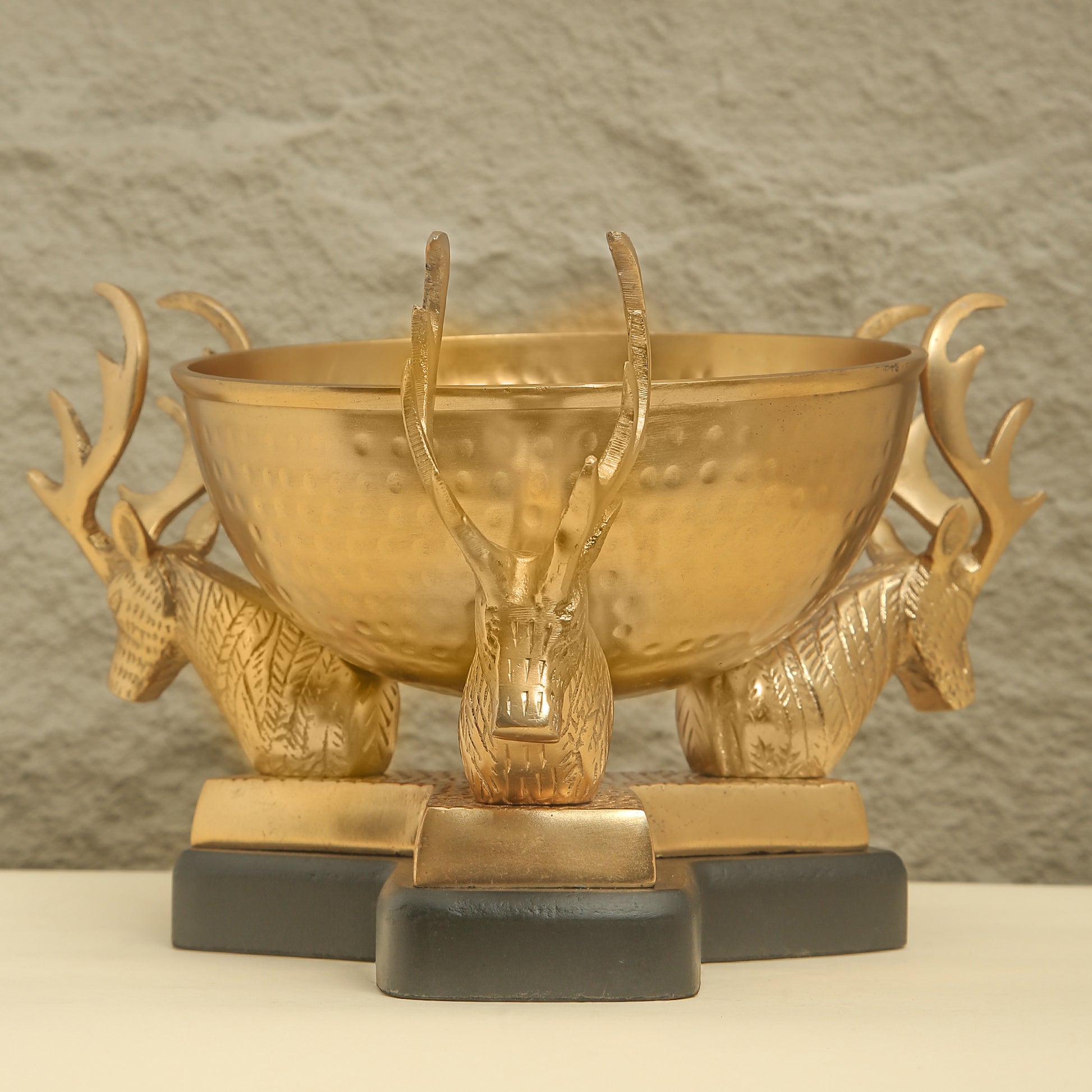 Gold bowl with deer head sculptures on a neutral background