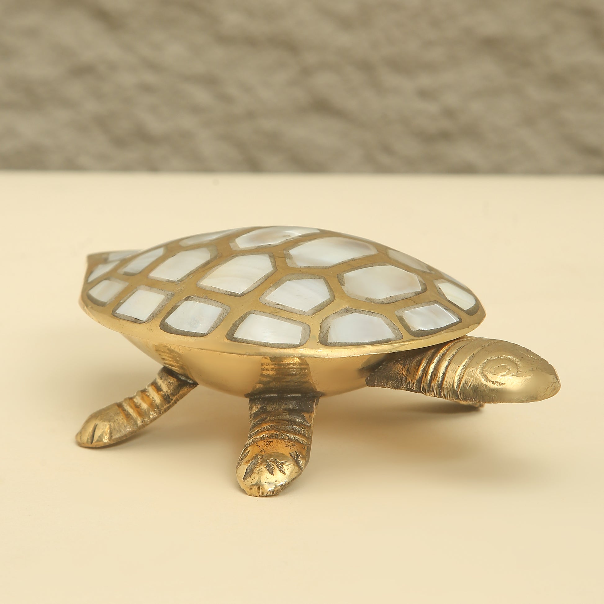 Brass turtle figurine with a checkered shell on a beige background