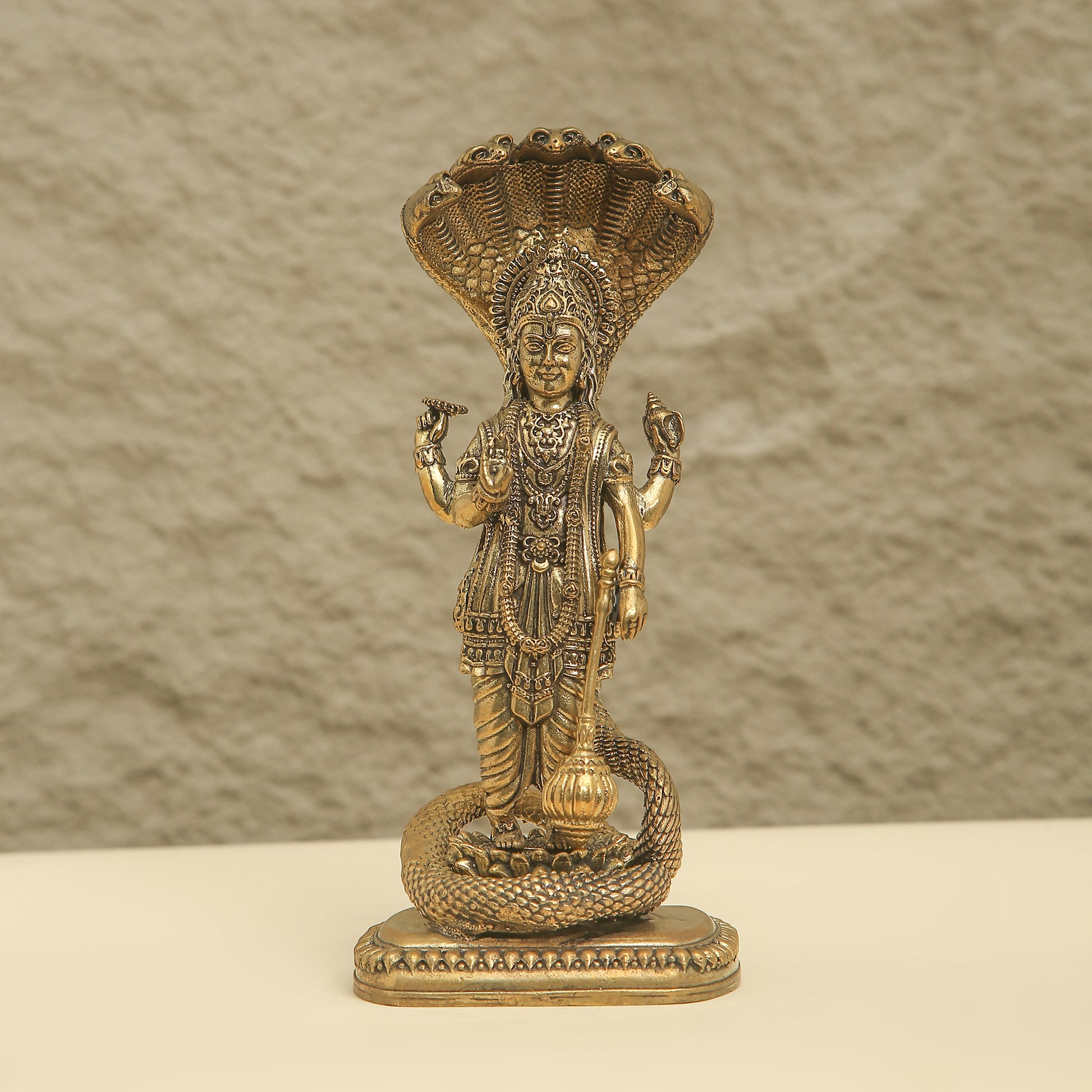 Gold-colored statue of a deity with intricate details on a textured beige background