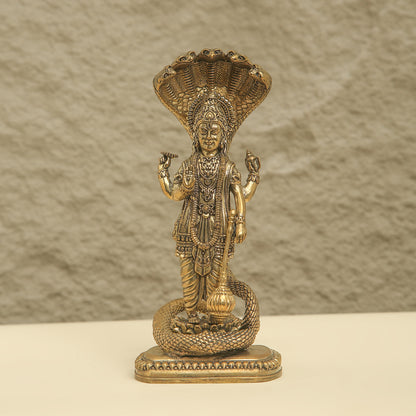 Gold-colored statue of a deity with intricate details on a textured beige background