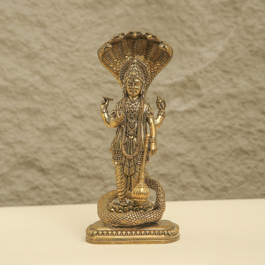 Gold-colored statue of a deity with intricate details on a textured beige background