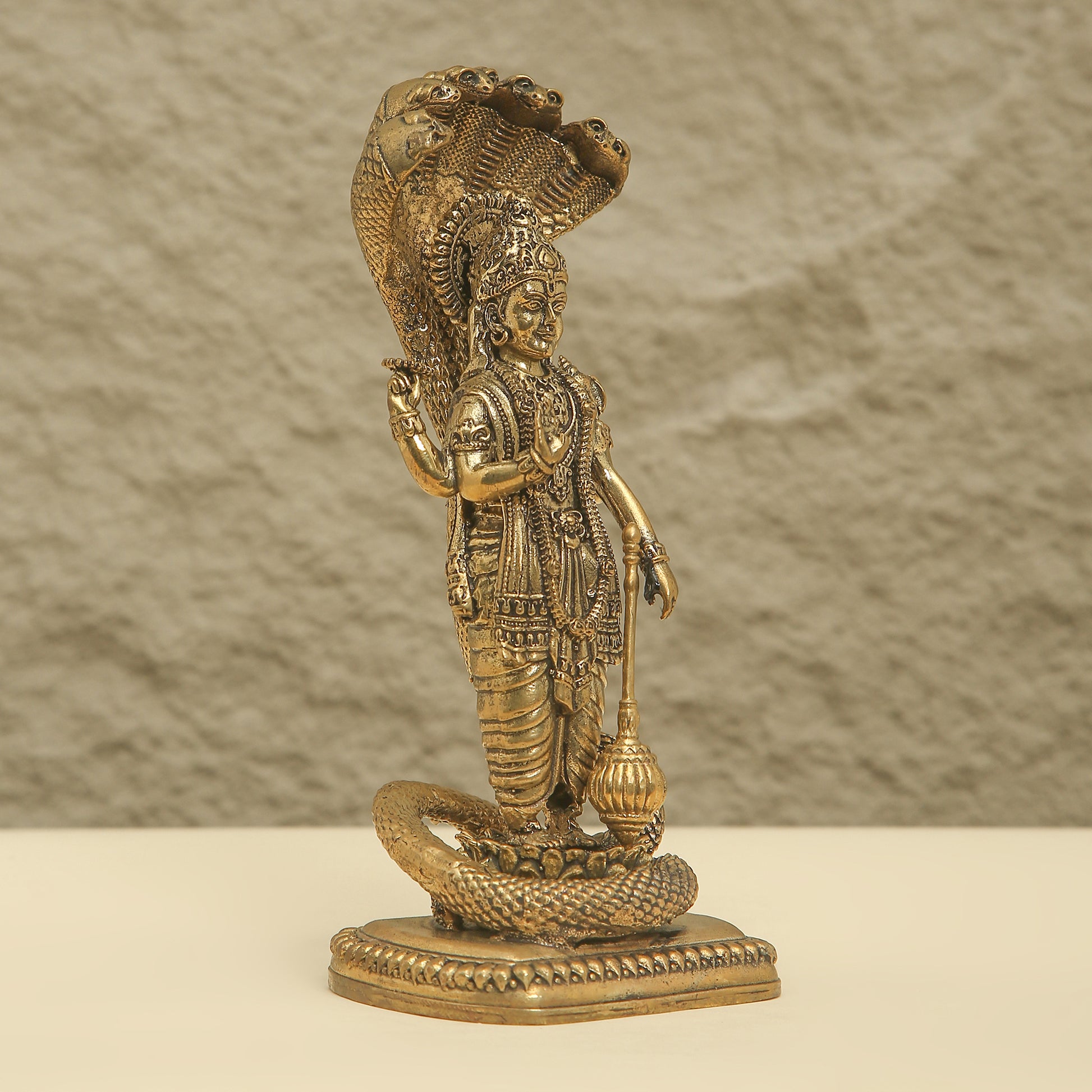 Bronze statue of a deity with a snake on a beige background