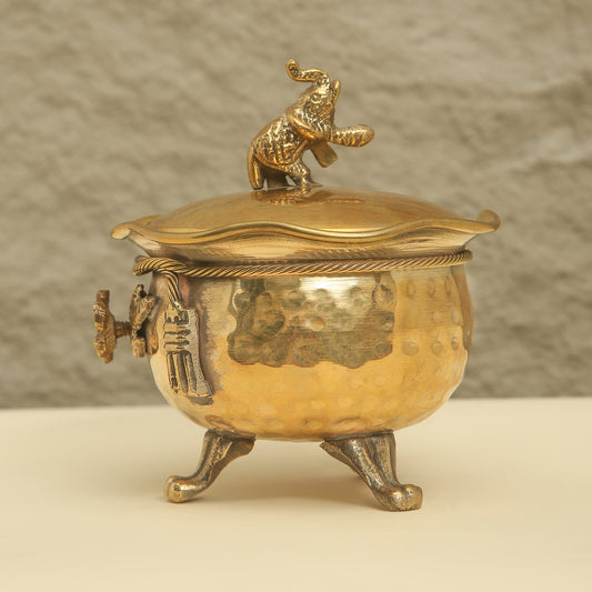 Gold-colored decorative container with a lid featuring a figurine on a beige background