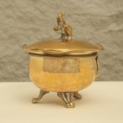 Gold-colored decorative container with a lid featuring a figurine on a beige background