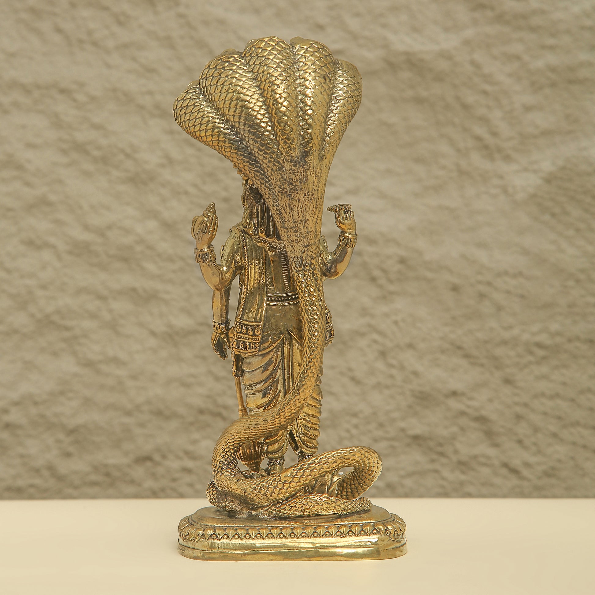 Bronze statue of a figure with a large snake draped over them against a textured beige background