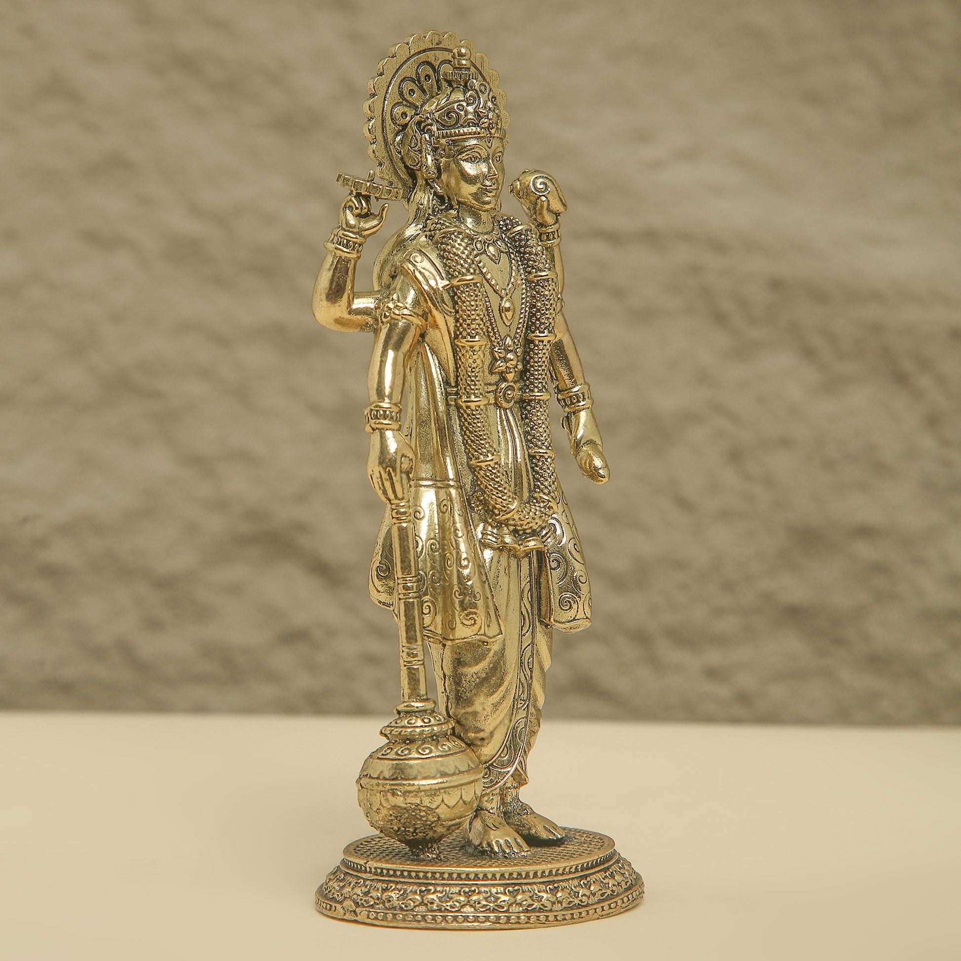 Gold-colored statue of a deity on a beige surface with a brown background