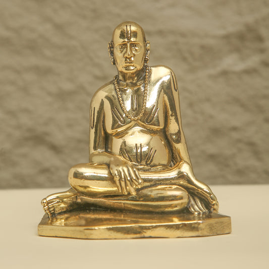 Gold statue of a seated figure on a beige surface with a neutral background