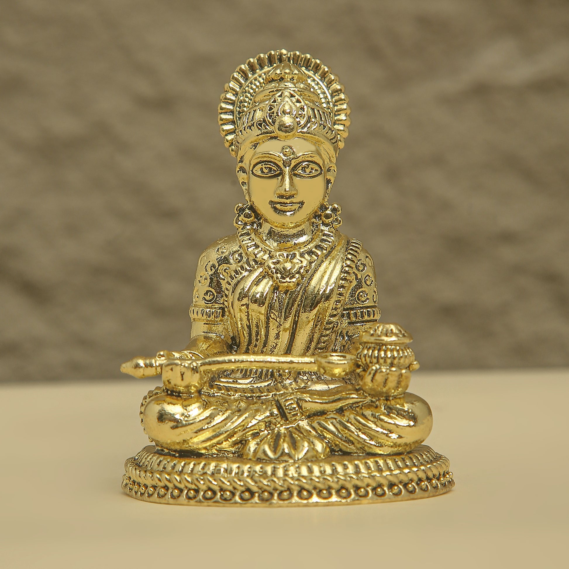 Gold-colored statue of a seated figure with intricate details on a beige background