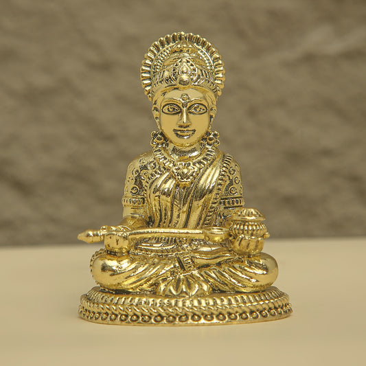Gold-colored statue of a seated figure with intricate details on a beige background