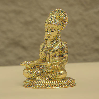 Gold-colored statue of a seated figure with intricate detailing on a beige background