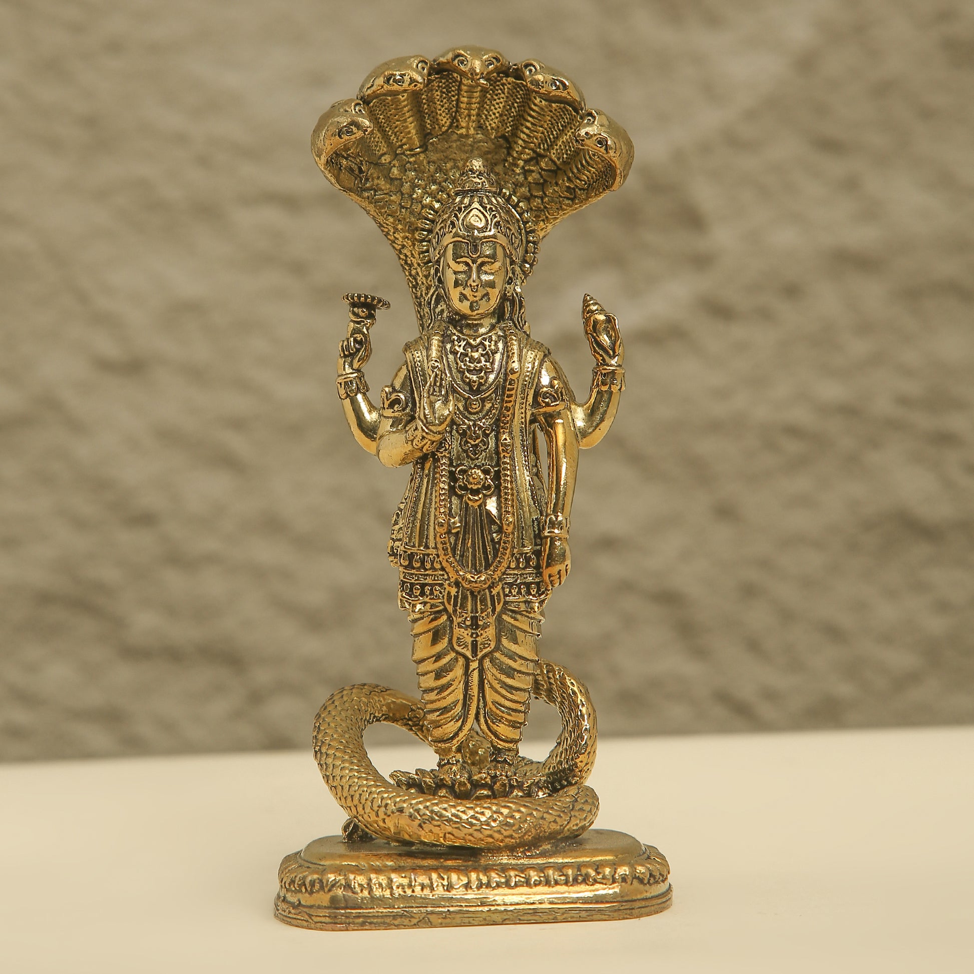 Brass statue of a deity with a snake on a beige background